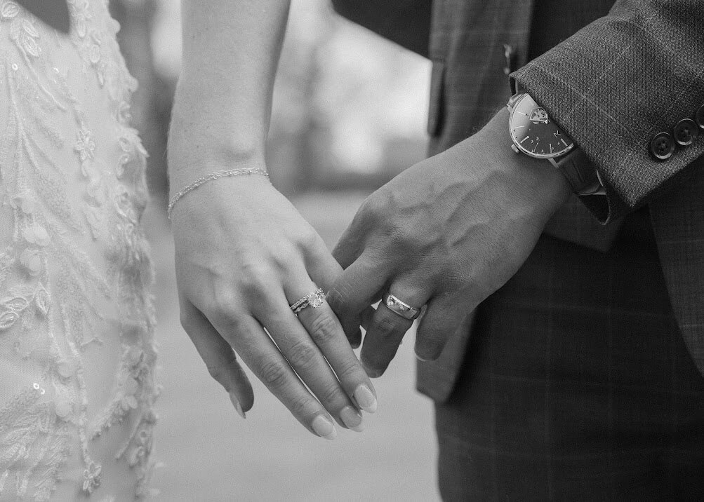 Black and white close up photo of groom holding onto brides pinky finger as they walk