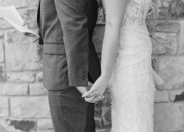 Black and white photo of bride and groom standing back to back to exchange private vows while holding hands