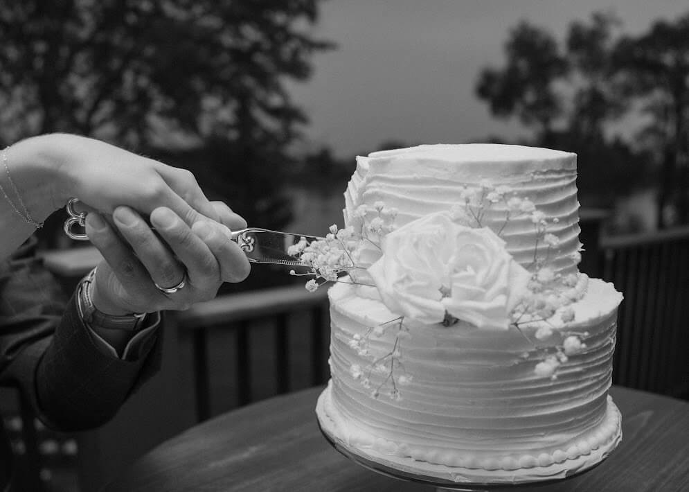 Black and white photo, close up shot of bride and groom holding a knife together as they take the first slice into their delicate two layered wedding cake
