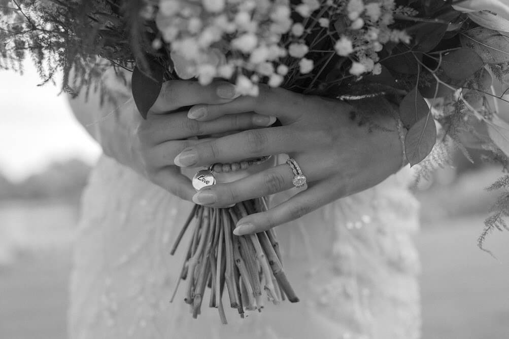 Close up photo of brides hands on her bouquet with her ring and lover charm displayed