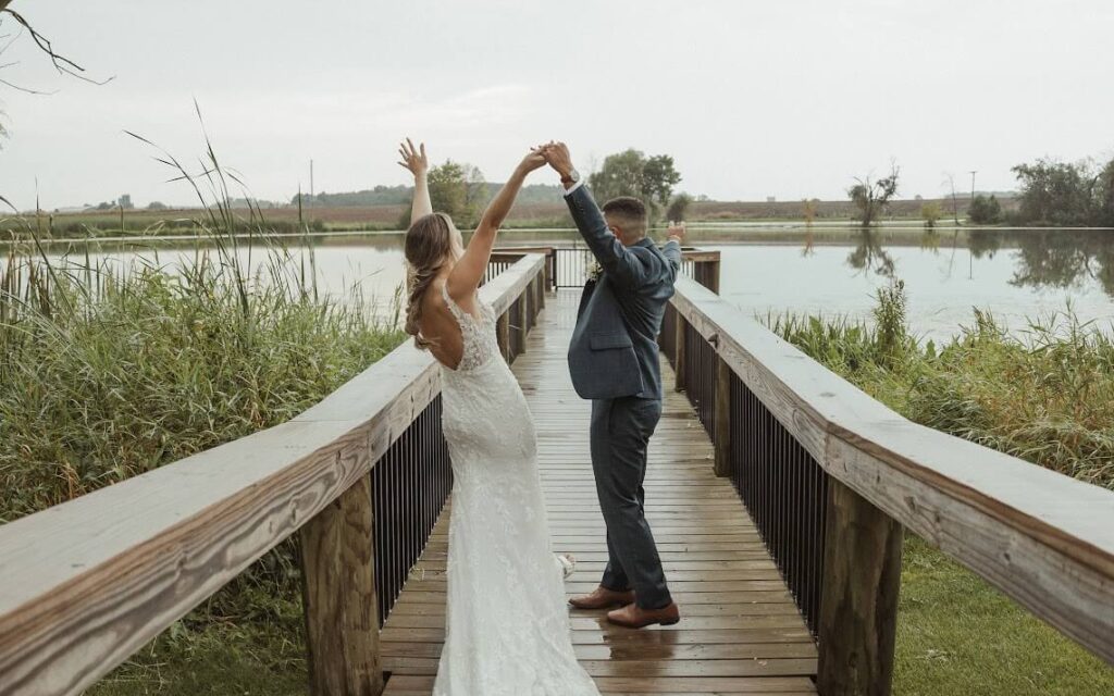 Bride and Groom standing on a dock with hands thrown up in celebration after ceremony